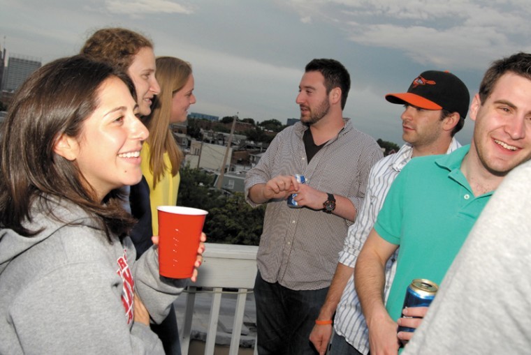 Moishe House Baltimore residents Jen Posner, left, and Mickey Rubin, wearing a Baltimore Orioles cap, host a rooftop barbecue for other young Baltimore Jews, May 19, 2011.