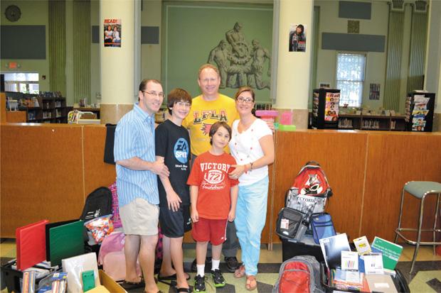 Caleb Pultman, his parents, Mimi and Andy Pultman, and brother Chase pose with Lift for Life Academy founder Marshall Cohen (center, in yellow shirt) with the school supplies donated during a collection for Caleb’s mitzvah project. Caleb also volunteered at the Harvey Kornblum Jewish Food Pantry and donated a portion of his bar mitzvah gift money to Herzl Camp Scholarship Fund. 
