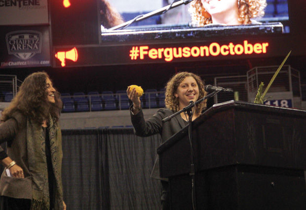 On Sunday night at Chaifetz Arena Rabbi Alana Alpert of Congregation T’chiyah and the Harriet Tubman Center in Detroit, holds the luluv and etrog as she speaks during a Ferguson October gathering. At left is Rabbi Susan Talve of Central Reform Congregation. Photo: Philip Deitch