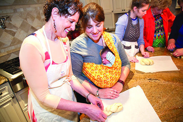 Julie Eisenberg (left) and Alana Minoff (carrying son Yishama) make challah together during a Loaves of Love baking session at Eisenberg’s home in late April. 