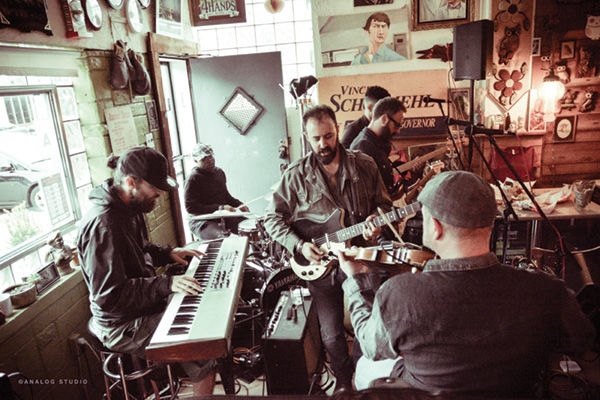 Photo taken recently at the Tick Tock Tavern, 3459 Magnolia Ave, St. Louis. L-R clockwise from left: Nate Carpenter, keyboards; Grover Stewart, drums; Teddy Brookins, bass (partially obscured behind Jeff); Jeff Lazaroff, vocals and guitar; David Lazaroff, vocals and guitar; and Mark Hochberg, violin and sound design. Photo: Annie Martineau