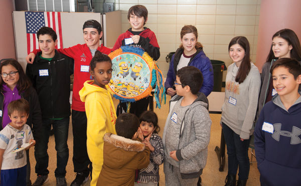 Aden Sher (holding pinata), Lilly Houser (in blue coat) and Jack Blase (at right) volunteered with members of the Shaare Emeth Temple Youth Group for a Winter Fun Day event held earlier this year for refugee families and children at the International Institute. The project was part Shaare Emeth’s “Hineni: Welcoming New Americans” program,  which has led to ongoing partnerships with the International Institute.  Photo: ANDREW KERMAN