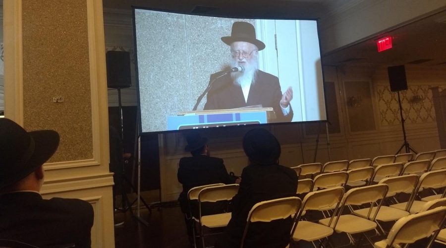 Rabbi+Hillel+Handler%2C+an+Orthodox+anti-vaccination+leader%2C+speaks+via+projection+screen+to+an+anti-vaccination+rally+in+Brooklyn+at+a+Jewish+wedding+hall%2C+June+4%2C+2019.+Photo%3A+Ben+Sales