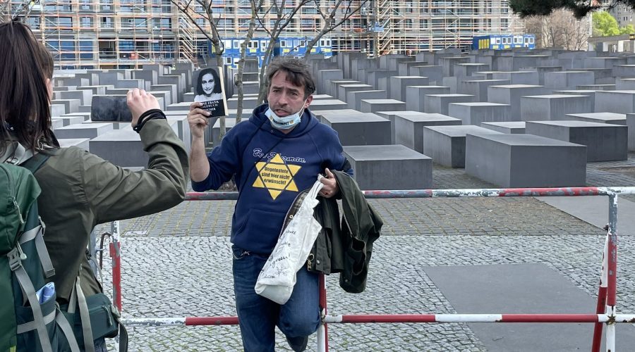 A+man+protests+coronavirus+restrictions+with+a+yellow+star+and+a+photo+of+Anne+Frank+outside+the+Holocaust+memorial+in+Berlin.+%28%40ZSKberlin%2FTwitter%29%0A