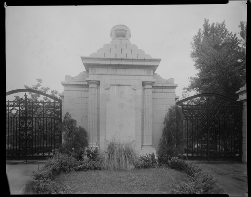 A close-up of the entrance gate at Chesed Shel Emeth Cemetery, located at 7570 Olive. There is a stone structure with two columns in between the two metal gate doors.