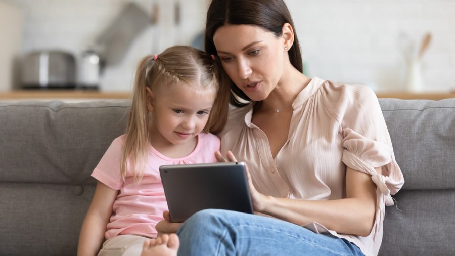 Mother teaching little daughter to use computer tablet close up