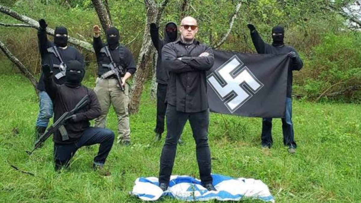 Neo-Nazi Christopher Pohlhaus stands on an Israeli flag while supporters make the Nazi salute and hold a swastika banner. 