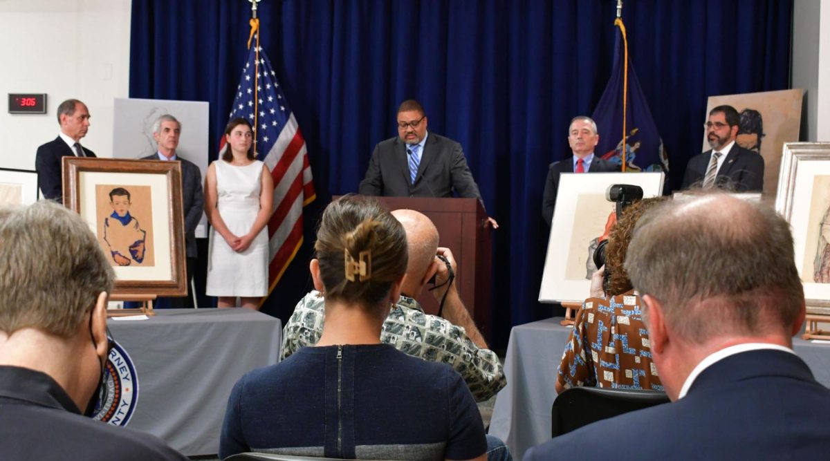 Manhattan district attorney Alvin Bragg, center, delivers remarks during a Sep. 20, 2023 ceremony to return stolen artworks to the heirs of Fritz Grünbaums estate: Timothy Reif, David Frankel, and Sarah Reif, left, pictured left to right. 
