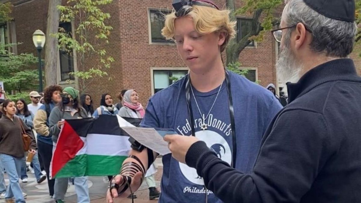 Rabbi Levi Haskelevich of Chabad at Penn helps a student don tefillin as a group of anti-Israel protesters passes by. Chabad.org's new survey finds that a wide spectrum of Jews are choosing to increase in acts of Jewishness as opposed to laying low and hiding their identity.