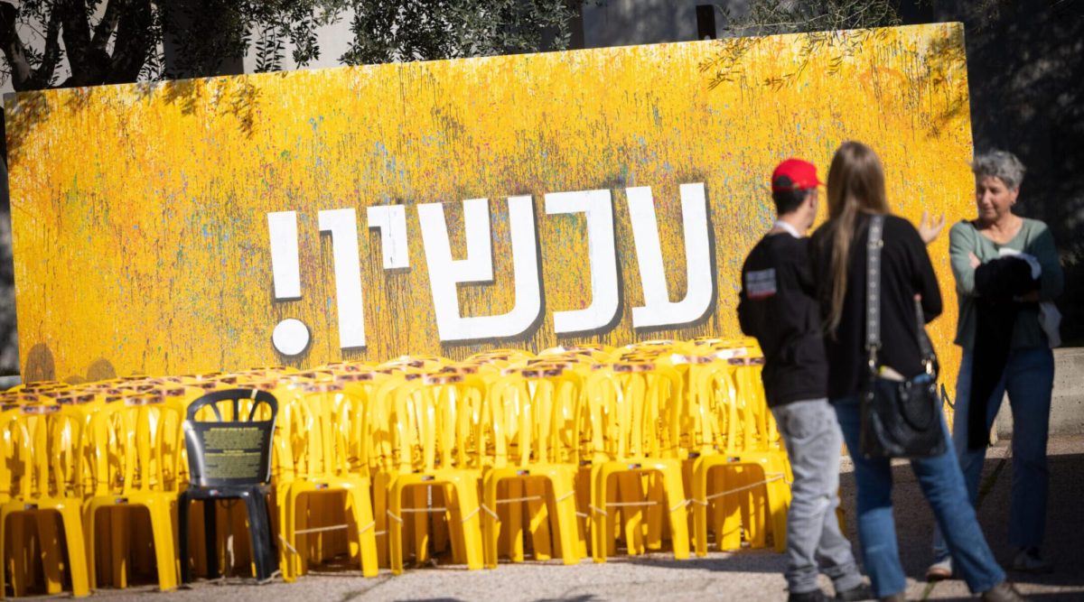 Visitors at Hostage Square in Tel Aviv stand in front of a sign reading "Now!" in Hebrew, Jan. 6, 2025. (Miriam Alster/Flash90)