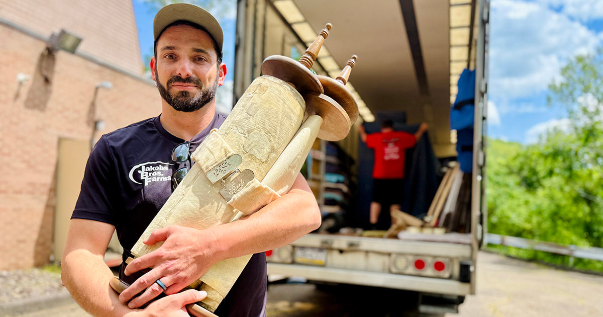 Nik Jakobs holding the Torah donated to him by Temple B’nai Israel in White Oak, Pennsylvania. A moving truck is in the background. Photo by Benyamin Cohen

