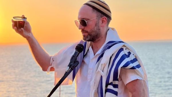 At sunset by the water, Rabbi Ari Yehuda Saks leads a blessing with wine in hand and tallit draped over the shoulders (Courtesy / Moti Dolgin)