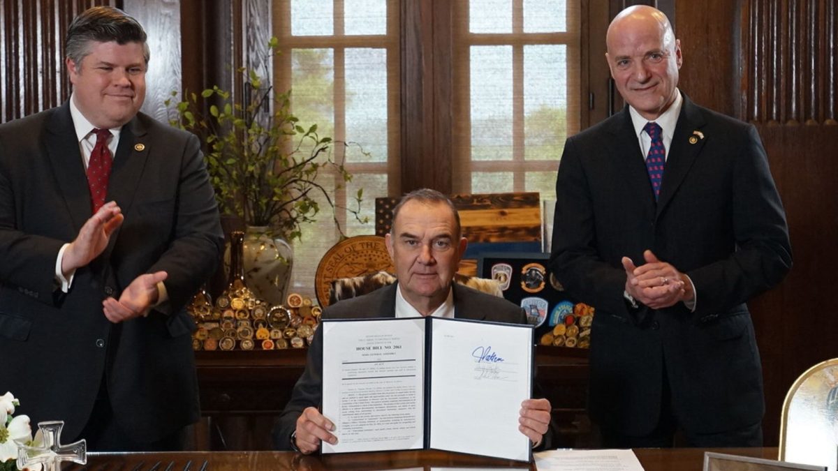 Missouri Governor Mike Kehoe signs HB 2061, with bill sponsors State Senator Curtis Trent (L) and State Representative George Hruza (R) looking on at the State Capitol, in Jefferson City, Missouri, April 23, 2026.